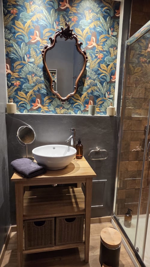 Élégant meuble de salle de bain au Manoir de la Bégaudière avec vasque blanche ronde, miroir orné et papier peint botanique bleu vibrant
