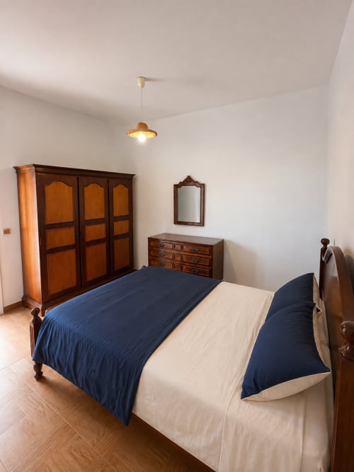Quarto espaçoso nas Villas Simone Porto Santo com cama de madeira, guarda-roupa, cômoda e iluminação pendente