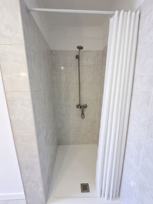 Banheiro de chuveiro moderno com paredes em azulejos cinza, chuveiro tipo chuva e cortina branca na Villas Simone Porto Santo