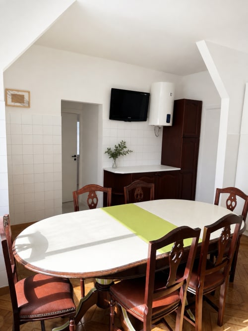 Área de refeições do apartamento familiar com mesa de madeira, cadeiras, kitchenette, televisão e paredes com azulejos brancos em Casa da Mãe, Porto Santo