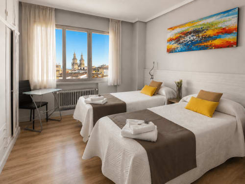 Amplia habitación doble con vistas a la catedral de Logroño en el hotel Muro 13 El Mirador, con ropa de cama blanca y escritorio de trabajo