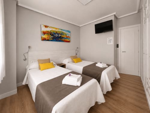 Habitación doble en Muro 13 El Mirador del Espolón de Logroño con camas blancas, almohadas amarillas, arte mural, TV y suelo de madera