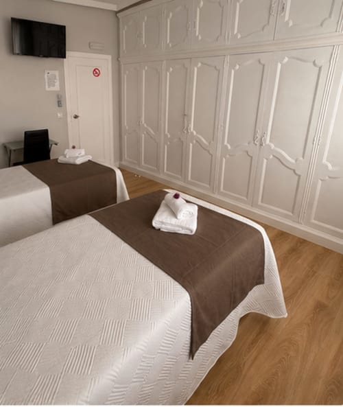 Moderno dormitorio doble en el hotel Muro 13 El Mirador del Espolón de Logroño con dos camas, suelos de madera y paneles blancos