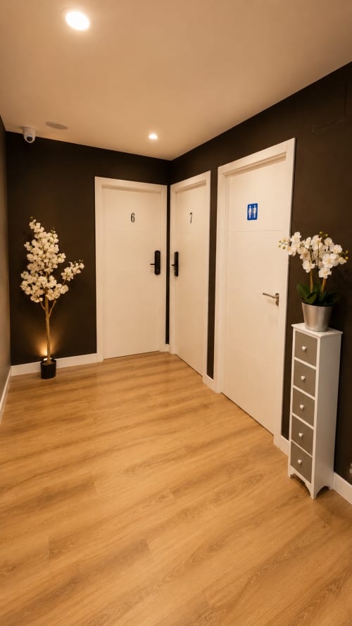 Elegante pasillo de hotel con puertas color crema numeradas 6 y 7, paredes oscuras, piso de madera, orquídeas blancas e iluminación ambiental