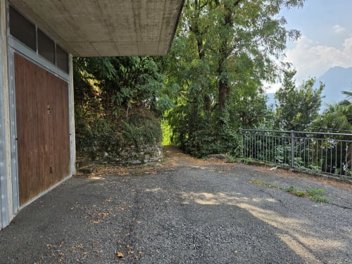 Covered terrace at Villa Vista Lago di Como in Bellano with wooden door, gravel patio, and lush garden views