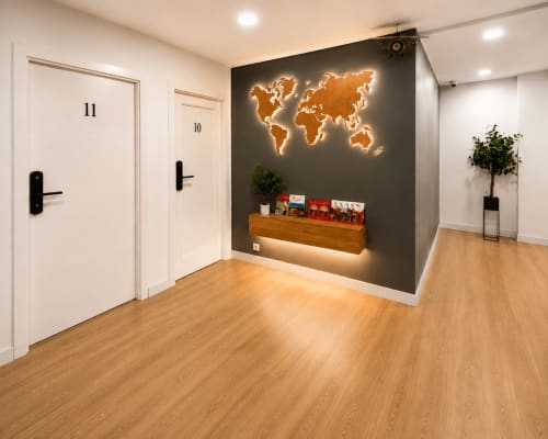 Moderno pasillo de hotel con mapa mundial iluminado, mueble de almacenamiento en madera, planta en maceta y puertas numeradas en Muro 13 El Mirador