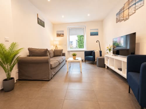 Salon moderne de la villa Mattbnb à Metz avec canapé marron, fauteuil bleu, télévision et vue sur la ville