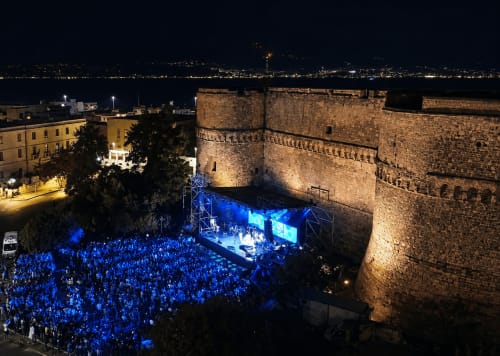 Concerto notturno a Reggio Calabria con fortezza medievale illuminata e luci costiere sullo sfondo