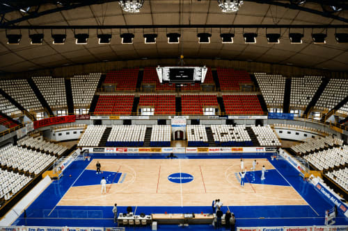 Arena sportiva di Reggio Calabria con campo di pallavolo blu, posti a sedere per migliaia di spettatori, illuminazione moderna