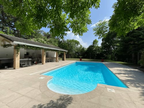 Resort swimming pool with blue water surrounded by stone patio, lounge areas, and lush green trees at Domaine de Bize in