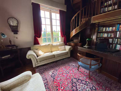 Suite Familiale élégante au Domaine de Bize Mirepoix avec canapé crème, escalier en spirale, rideaux rouges et bibliothèque boisée