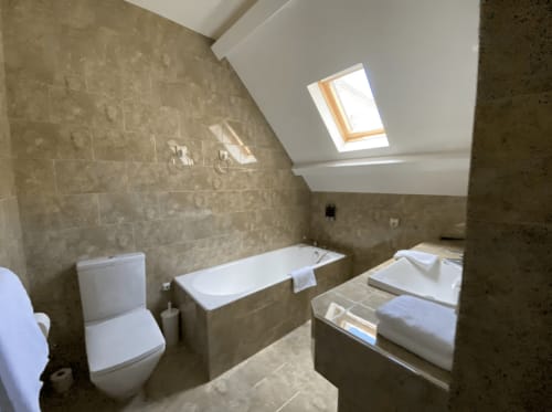 Modern attic bathroom at Domaine de Bize Mirepoix with white bathtub, toilet, skylight, and beige tile walls