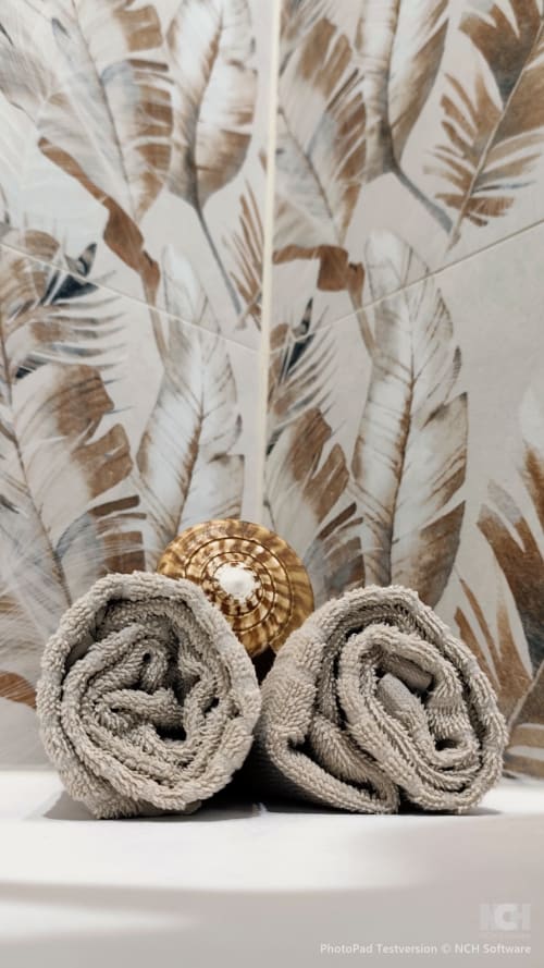 Aufgerollte beige Handtücher mit goldenem Dekorationsorament vor Vorhängen mit Federblattprunmuster im Apartment Fly High, Morro
