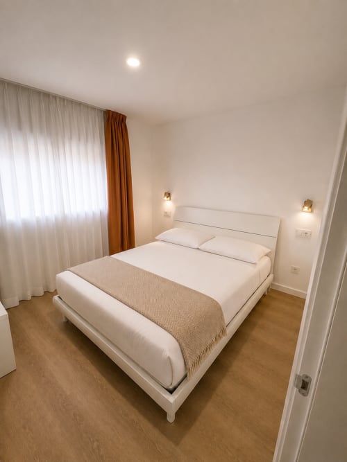 Modernes Schlafzimmer im Fly High, Morro Jable mit Queensize-Bett, weißer Bettwäsche, Holzböden und terrakottafarbenen Vorhängen