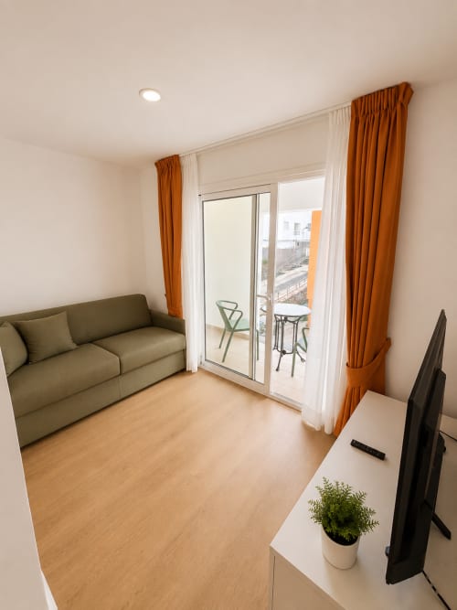 Modernes Wohnzimmer in Morro Jable mit Olivsofa, Holzböden, orangenen Vorhängen und Balkonzugang