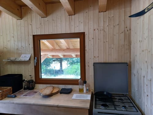 Cuisine chaleureuse d'une yourte à La Yourte Un Autre Monde avec intérieur bois, cuisinière à gaz et vue montagne par la fenêtre