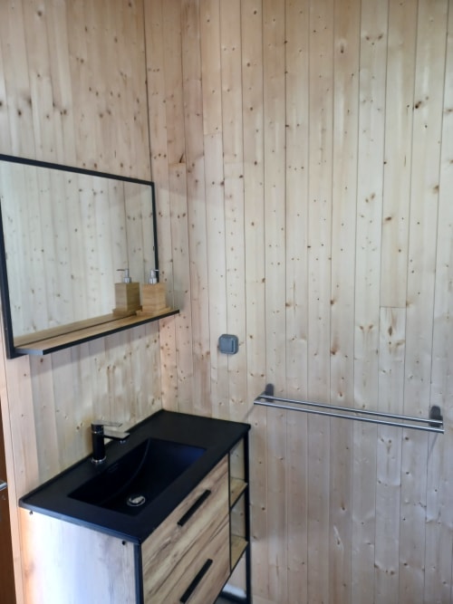 Salle de bain moderne de la yourte La Yourte Un Autre Monde avec murs en bois, lavabo noir, miroir et étagère au Hohwald