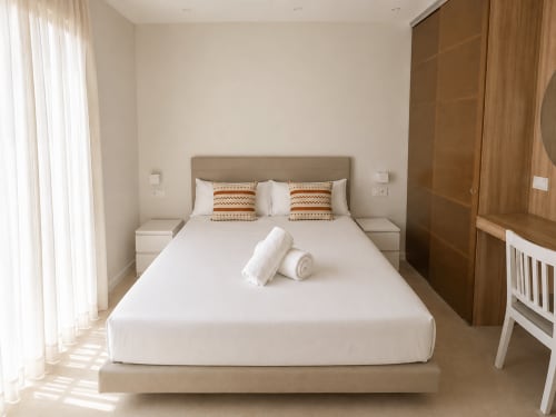 Dormitorio moderno en apartamento Sabaris con cama queen, ropa de cama blanca, armario de madera y acceso a terraza