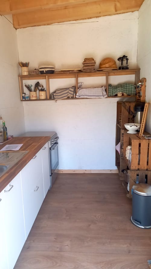 Cuisine chaleureuse de la yourte à La Yourte Un Autre Monde au Hohwald, avec étagères en bois, placards blancs et décoration rustique