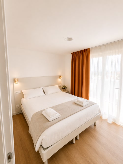Modernes Schlafzimmer im Fly High Hotel in Morro Jable mit weißem Bett, orangenen Vorhängen, Holzböden und Meerblick