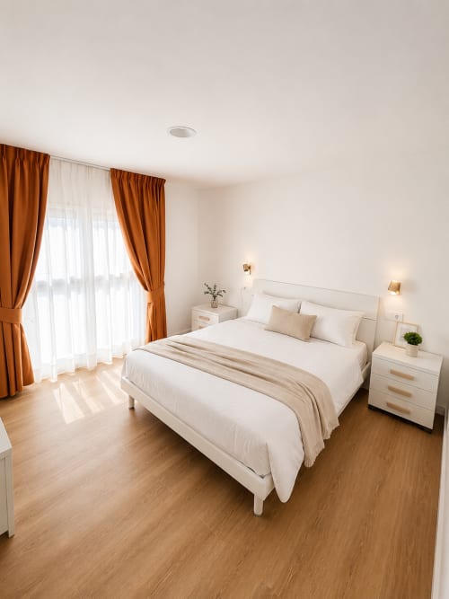 Helles Schlafzimmer mit Meerblick im Fly High Hotel in Morro Jable mit weißem Bett, orangenen Vorhängen und Holzböden