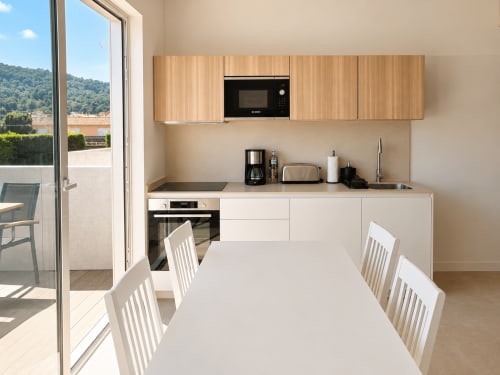 Moderna cocina y comedor en apartamento Sabaris con vista a terraza, sillas blancas, muebles de madera y