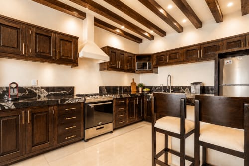 Modern kitchen with dark wood cabinets, black granite countertops, stainless steel appliances, and exposed beams at Casa