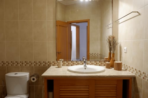 Banheiro moderno no townhouse Be SilverCoast com pia redonda, móvel em madeira, azulejos bege e espelho em Serra D'El Rei