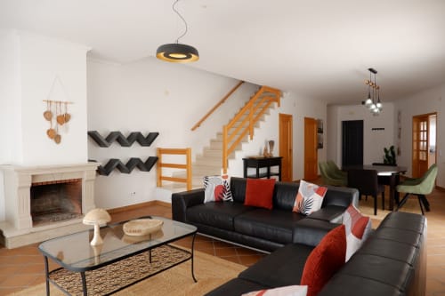 Sala de estar moderna em townhouse Be SilverCoast com sofá preto, lareira, escadas de madeira e vistas para o mar em Serra D'El Rei