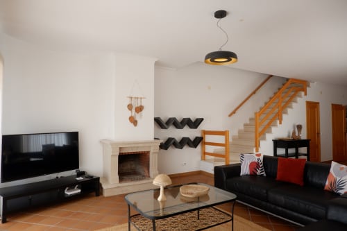Sala de estar moderna com sofá preto, lareira, TV e escada de madeira na townhouse Be SilverCoast em Serra D'El Rei