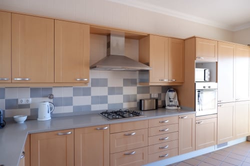 Cozinha moderna com armários de madeira, bancadas cinzas, fogão a gás e azulejos de padrão xadrez azul na casa de vila Be SilverCoast
