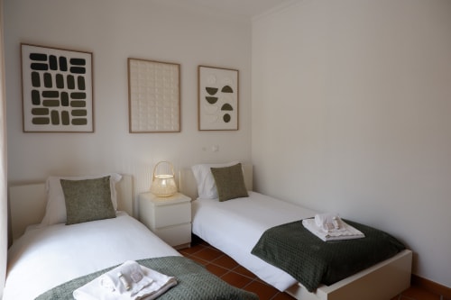 Duas camas de solteiro com almofadas oliváceas no quarto minimalista da casa de vila Be SilverCoast, arte de parede discreta e luminária pendente