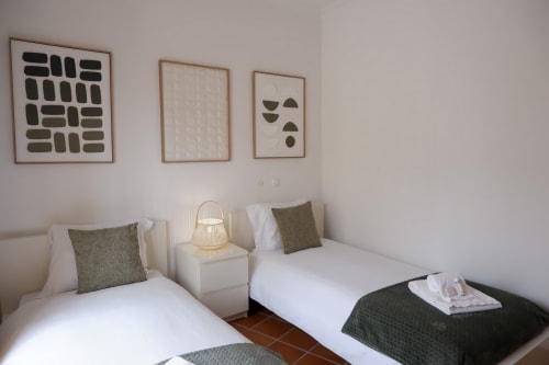 Quarto com duas camas na unidade Be SilverCoast, Serra D'El Rei, Portugal, com roupa de cama branca, almofadas verde-azeite e design moderno