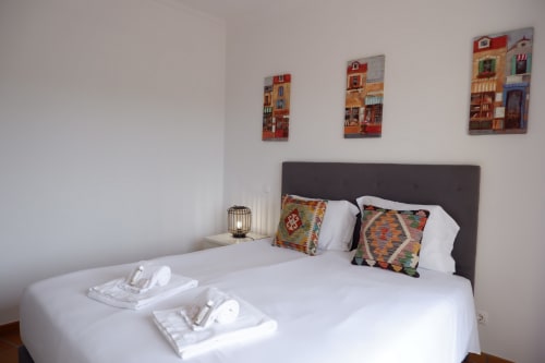 Quarto com cama branca, almofadas coloridas e três quadros de casarões em Be SilverCoast em Serra D'El Rei, Portugal