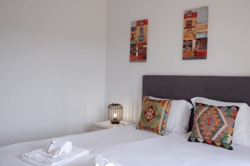 Quarto aconchegante da casa Be SilverCoast em Serra D'El Rei com almofadas coloridas, cabeceira escura e obras de arte costeira