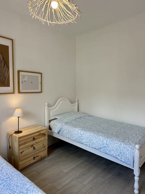 Chambre lumineuse aux Villas Simone Porto Santo avec lit blanc, table de nuit en bois, lampe et tableaux encadrés