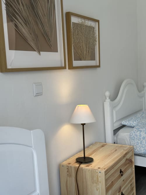 Coin de chambre à Villas Simone Porto Santo avec table de nuit en bois, lampe de chevet, tête de lit blanche et botanical encadré