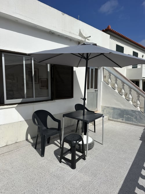 Terrasse ensoleillée aux Villas Simone Porto Santo avec parasol noir, table et chaises donnant sur immeuble blanc