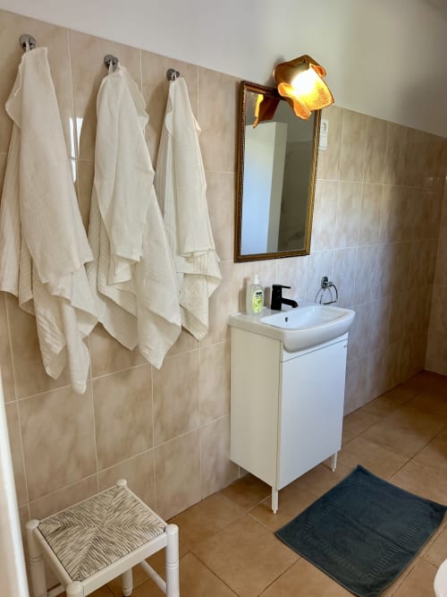 Salle de bain immaculée aux Villas Simone Porto Santo avec lavabo blanc, miroir, porte-serviettes et murs carrelés