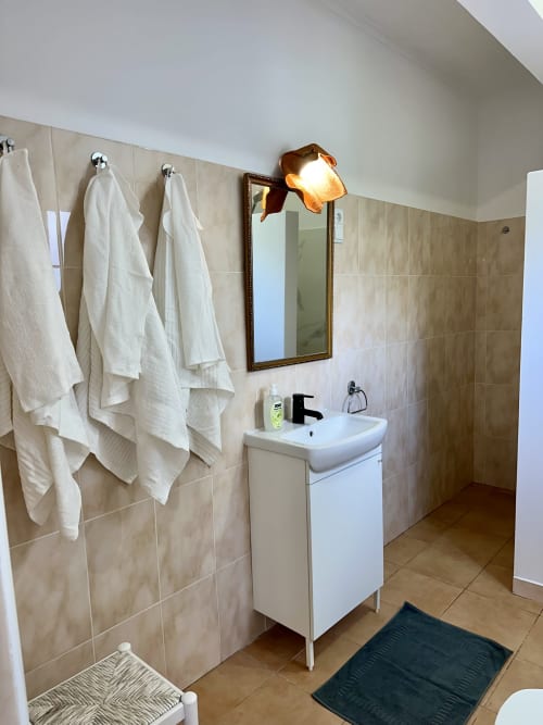 Salle de bains moderne aux Villas Simone Porto Santo avec vasque blanche, carrelage mural, miroir et serviettes blanches fraîches