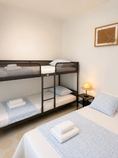 Quarto de família com beliche, cama individual, lençóis brancos e luminária na Villas Simone Porto Santo
