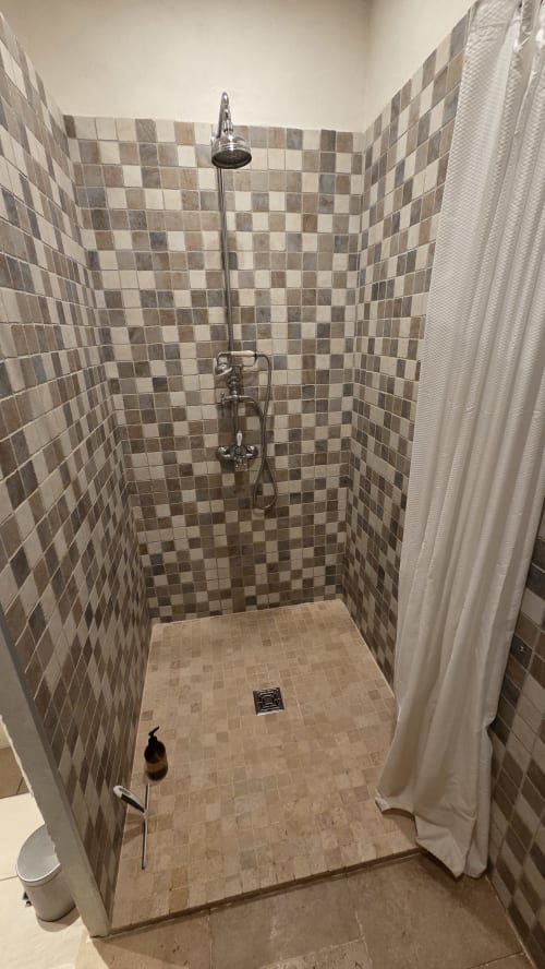 Douche commune au Manoir de la Bégaudière avec carrelage à motifs damier, pommeau de douche pluie et rideau blanc