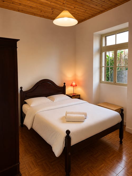 Quarto aconchegante no apartamento Casa do Taxista em Porto Santo com cama de madeira escura, lençol branco e iluminação ambiente acolhedora