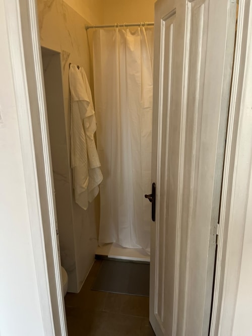 Banheiro compartilhado na Villas Simone Porto Santo com box de chuveiro, cortina creme, toalheiro e piso escuro