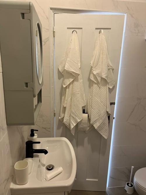 Banheiro moderno com pia branca, torneiras pretas e toalhas creme penduradas em ganchos do apartamento Casa do Taxista no Porto