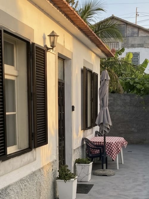 Terraço de apartamento em Porto Santo com mesa, cadeiras, guarda-chuva e plantas em vasos junto a edifício cor creme