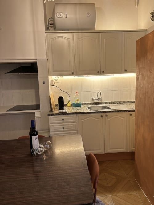 Cozinha moderna com armários bege, bancada de granito, mesa de jantar e garrafa de vinho no apartamento Casa do Taxista no Porto