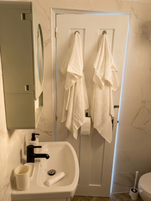 Banheiro moderno nas Villas Simone Porto Santo com pia branca, torneiras pretas e toalhas creme penduradas em ganchos na parede