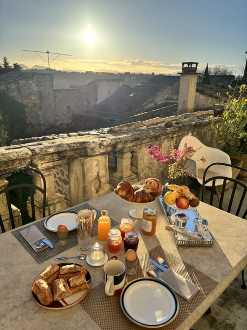 Table du petit-déjeuner à La vie de château B&B à Grignan avec croissants, fruits et vue sur le village