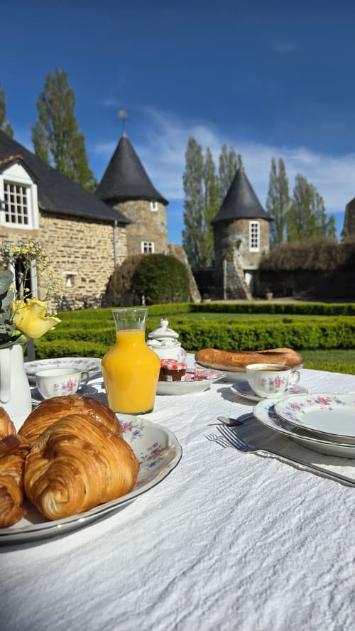 Outdoor breakfast at Manoir de la Bégaudière in Mont-Dol with croissants, juice, and castle towers in background